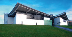 A large white building with a green roof is situated on a grassy field. AI generated content