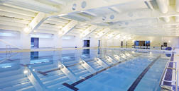 A large indoor swimming pool with a white ceiling and blue water. AI generated content